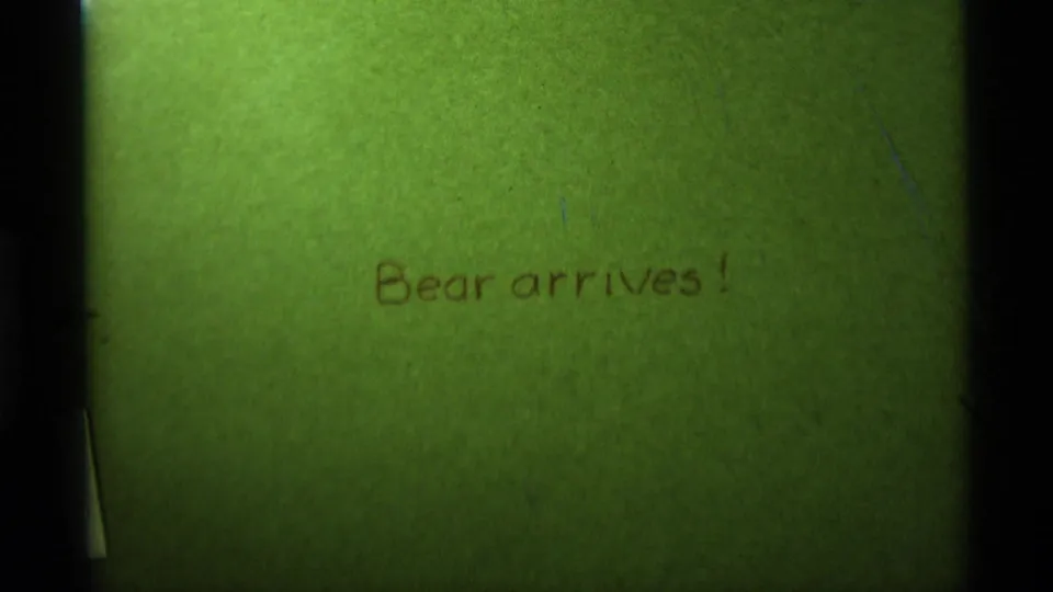 Green-tinted home-movie title card with brown handwritten text reading Bear arrives!, from the 1975 Montana clip metadata.