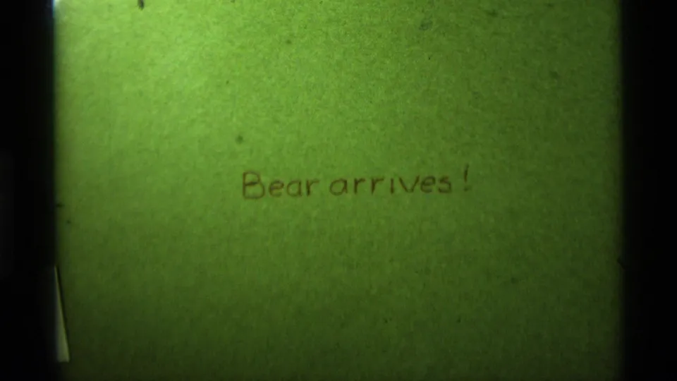 Green paper title card filling the frame, with handwritten brown text reading Bear arrives! and visible small-gauge film texture.
