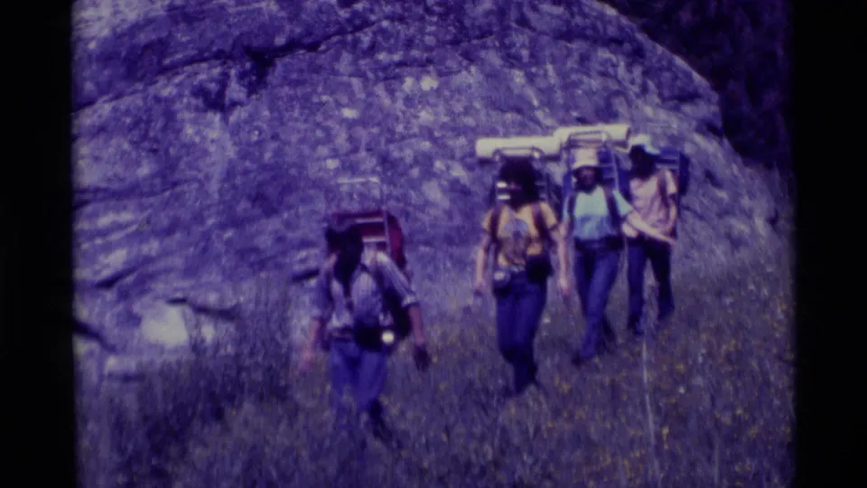 Four hikers with external-frame packs and rolled pads walk near the camera in the 1975 Agate Springs, Montana clip.