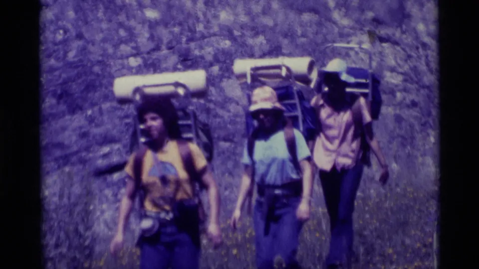 A closer 1975 Montana frame shows three of the hikers with backpacks and hats, with the fourth partly out of view.