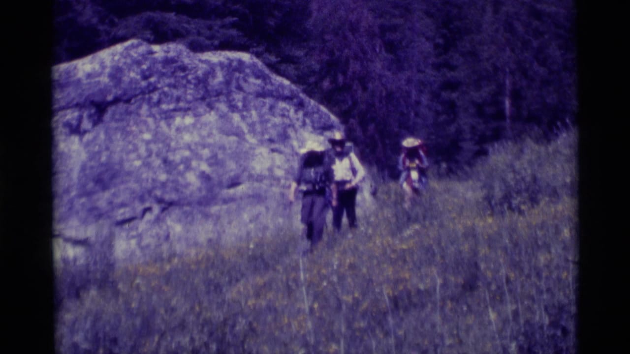 Three hikers in hats and backpacks walk through a grassy wooded trail in Agate Springs, Montana, in 1975 home-movie footage.