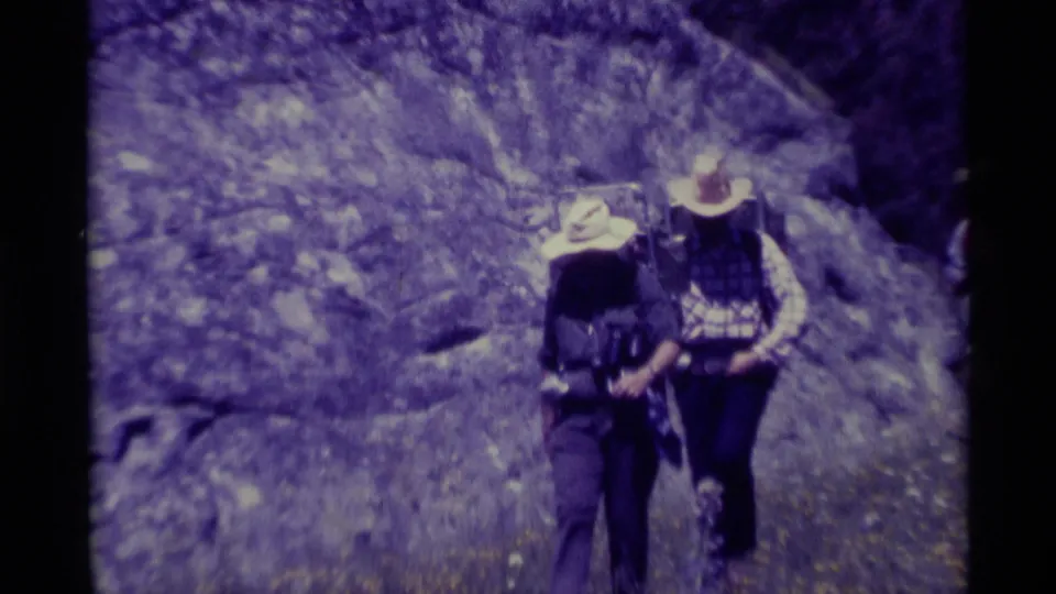 Two backpackers approach the camera near a rocky wooded slope in the 1975 Agate Springs, Montana home movie.