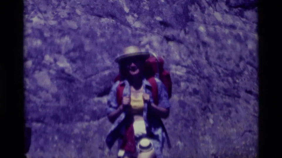 A hiker in Agate Springs, Montana, appears with a pack and brimmed hat, framed by purple-tinted 8mm film and rugged rock.
