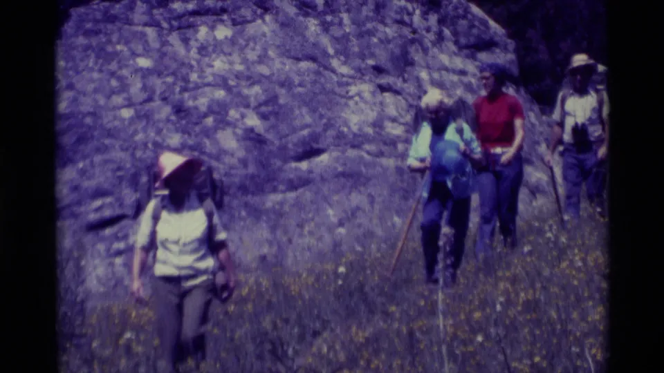 1975 Agate Springs, Montana frame with a lead hiker in a brimmed hat and three backpacked hikers following across the hillside.