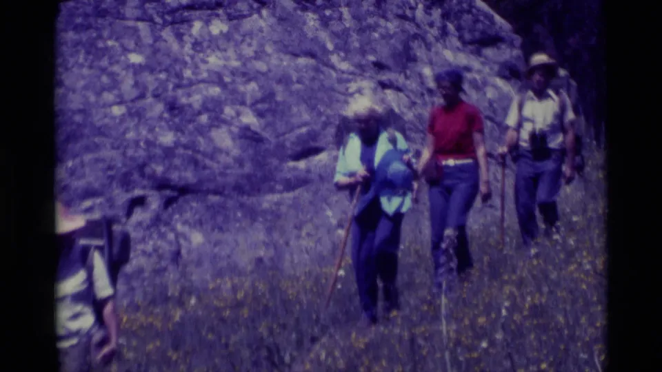 1975 Agate Springs, Montana frame showing backpacked hikers with walking sticks moving past wildflowers, with one figure partly out of frame.