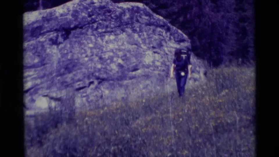 In 1975 Agate Springs, Montana footage, a woman hiker approaches from a distance below a large rock face.