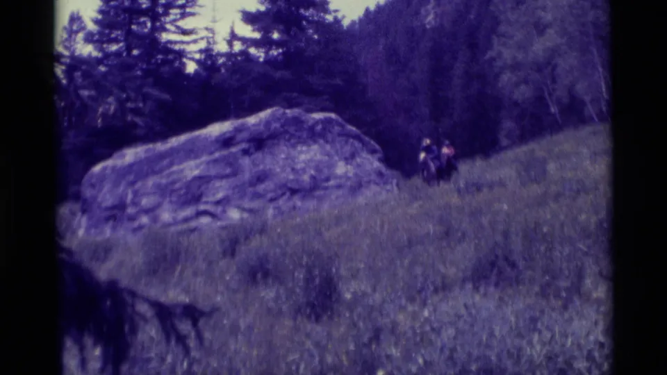 A faded 8mm frame shows two horseback riders near the boulder, with evergreen trees and hillside grass in Agate Springs metadata context.