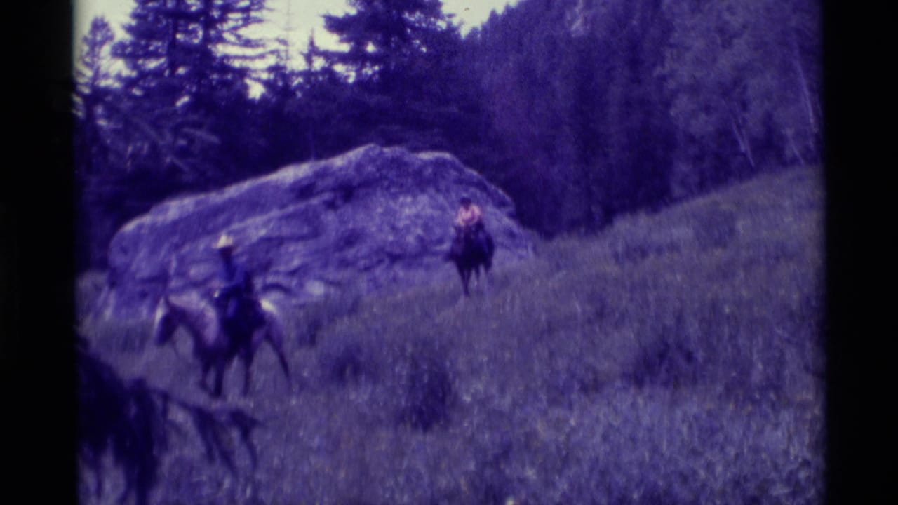 Horseback riders continue along the hillside with a large rock behind them.