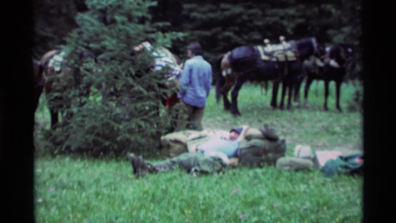 1975 Agate Springs, Montana home-movie frame showing a man resting on gear in a grassy wooded area with saddled horses behind him.