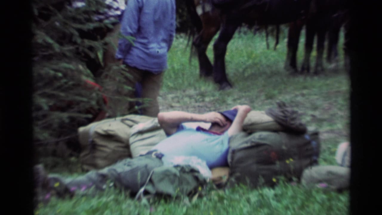 Closer view of a man lying on gear with horses and a standing person in the background.