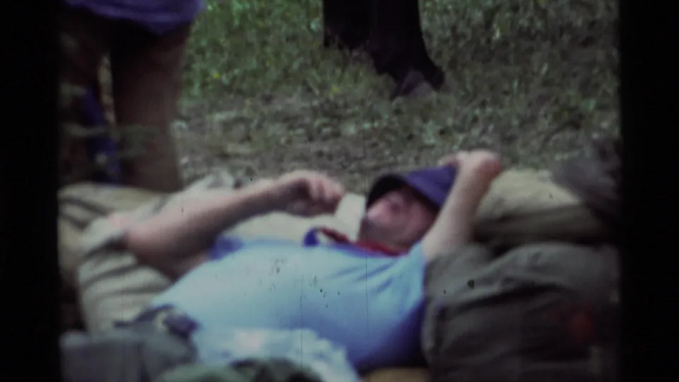Soft 8mm close-up from Agate Springs, Montana showing a man in a dark hat lying back on piled outdoor gear.