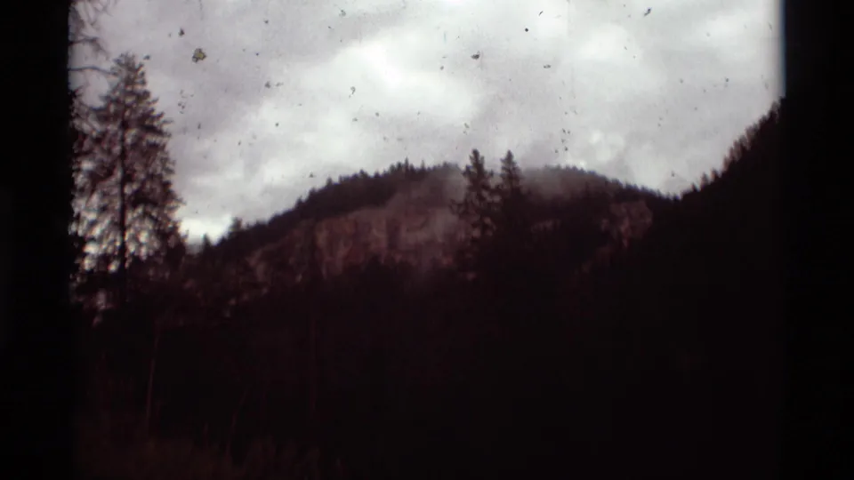 1975 8mm frame from Agate Springs, Montana, showing a misty ridge above dark evergreen woods with visible film dust.