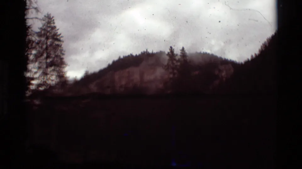 1975 8mm home-movie frame showing a dark Montana mountain hillside and trees under an overcast sky.