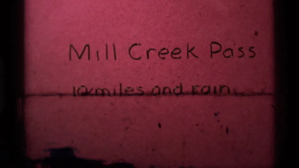 1975 8mm frame of the Mill Creek Pass title card, partly crossed by a dark horizontal film or scan mark.