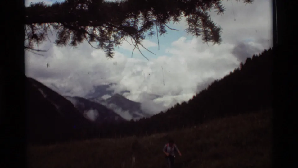 Soft 8mm home-movie frame from Agate Springs, Montana, showing a clouded mountain valley and a distant person low in the meadow.