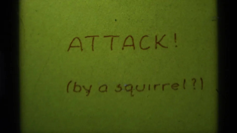 Handwritten 1975 home-movie title card on green paper reading ATTACK! with a parenthetical squirrel question.