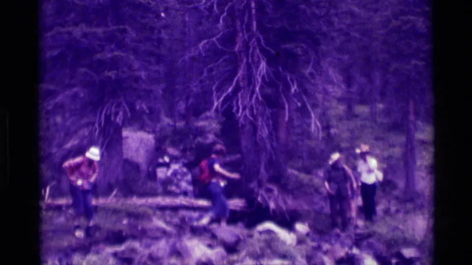 A small hiking group appears on a rocky forest path in Agate Springs, Montana, with one person in a white hat and another in a red shirt.
