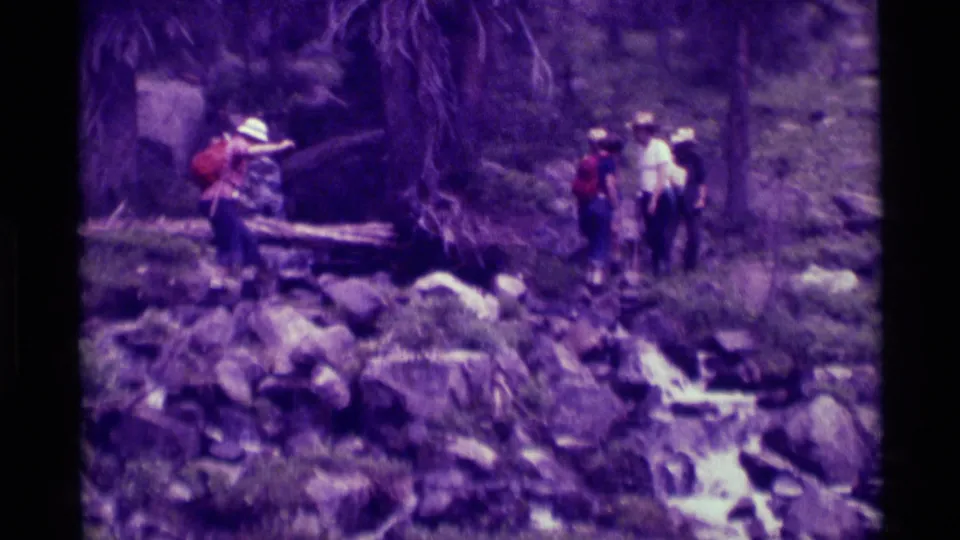 1975 8mm frame from Agate Springs, Montana, with several hikers gathered on a rocky trail beside a narrow stream.