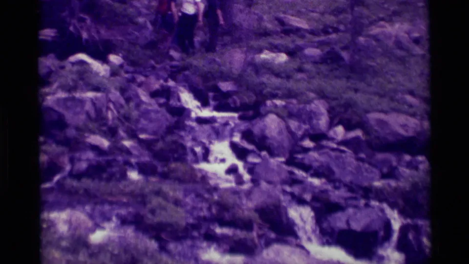 1975 8mm home-movie view near Agate Springs, Montana, focused on a rocky flowing stream with a hiker partly visible above.