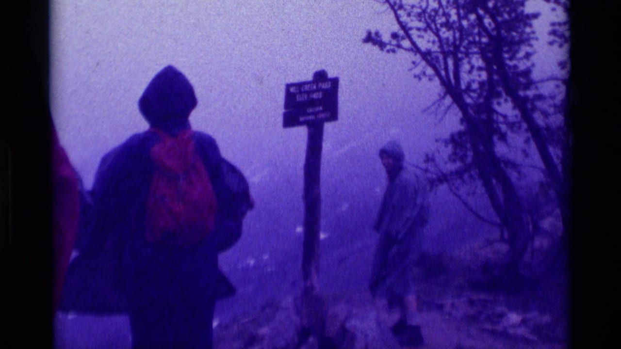 1975 Montana 8mm frame of a hooded hiker with red backpack near the Mill Creek Pass sign in Gallatin National Forest fog.