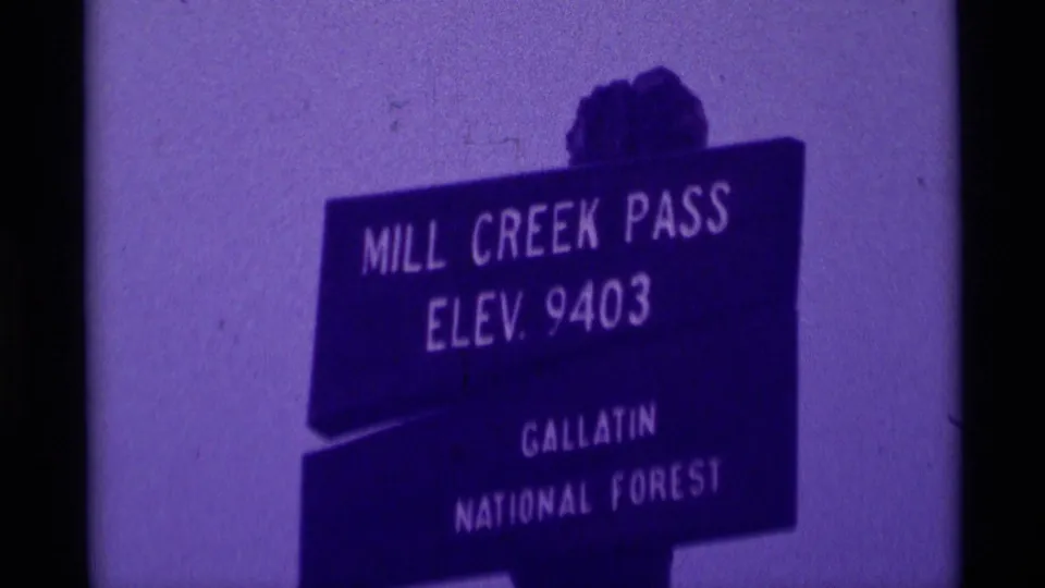 Tight 1975 8mm frame of the Mill Creek Pass elevation sign, with Gallatin National Forest text visible through purple haze.