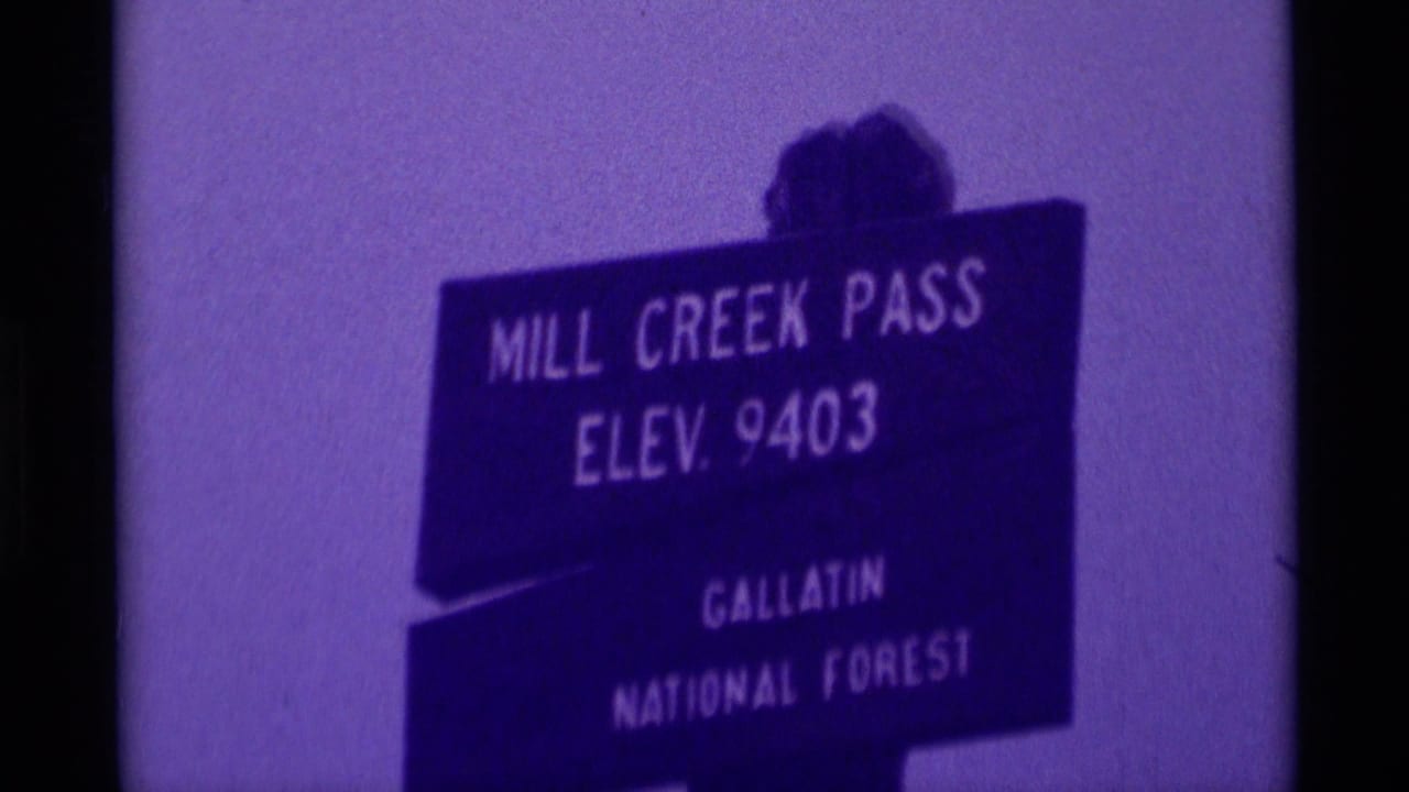 1975 8mm frame of the Mill Creek Pass sign reading elevation 9403 in Gallatin National Forest, seen through soft purple film color.