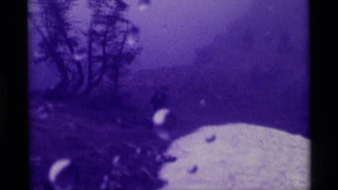 1975 8mm frame from Agate Springs, Montana showing a purple-cast rainy mountainside with trees, snow patches, and lens droplets.