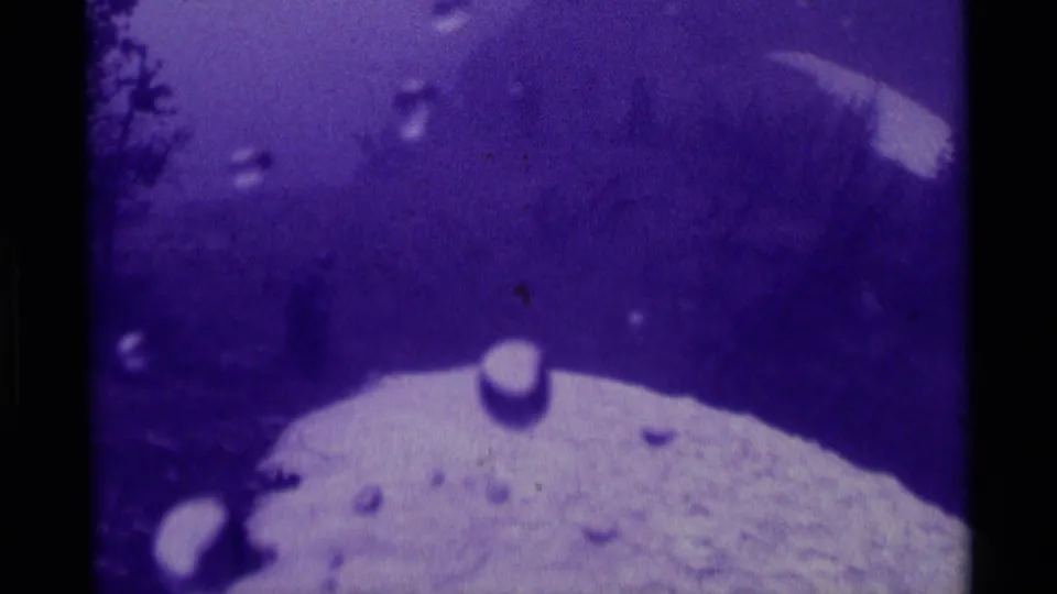 Purple-tinted 1975 Montana 8mm frame with rain on the lens, pale snow, dark trees, and a hazy mountain backdrop.