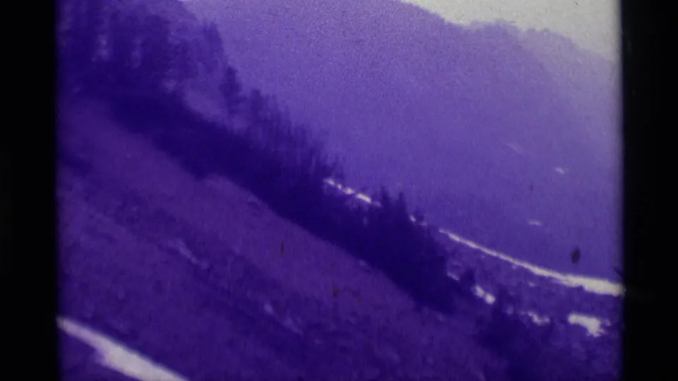 1975 Agate Springs, Montana frame with a dark tree band crossing a snow-streaked mountainside beneath a hazy ridge.