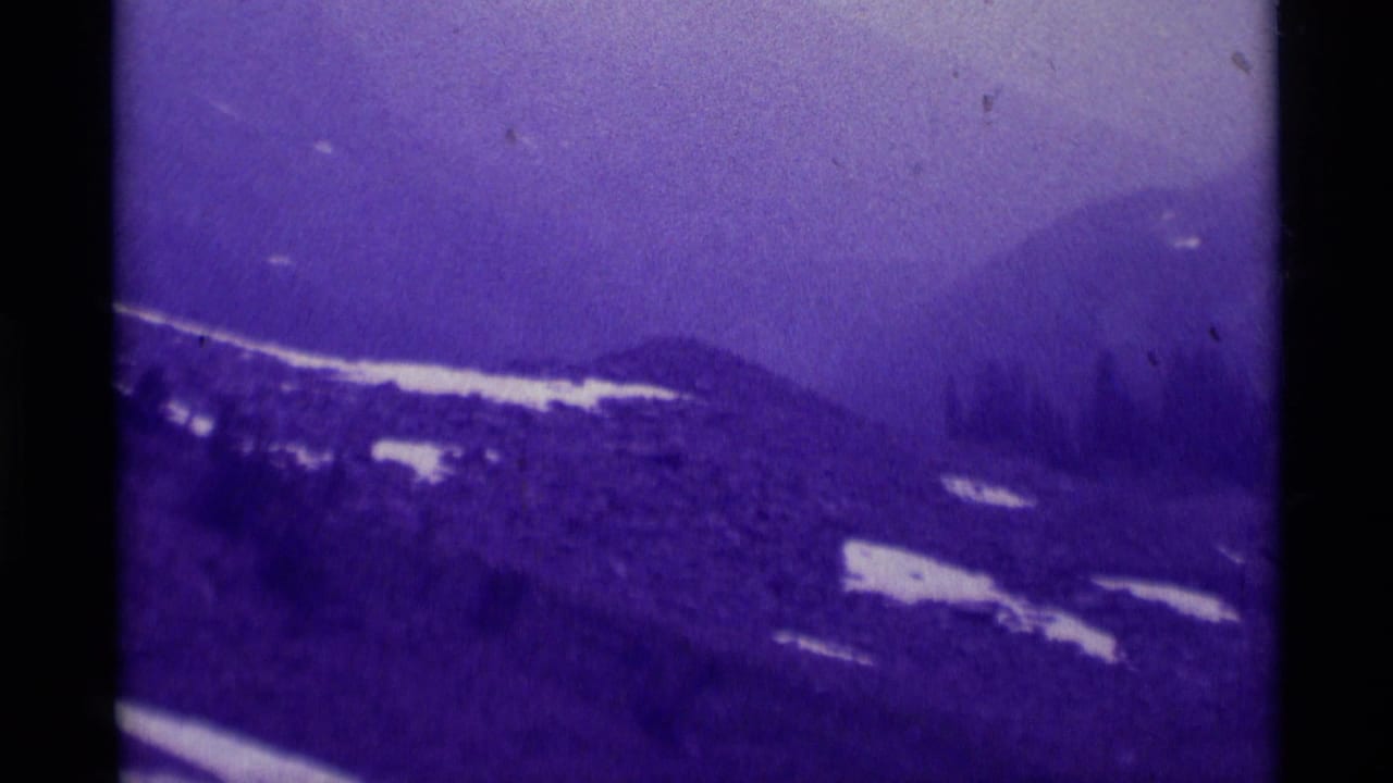 1975 Montana 8mm view of foggy mountain slopes, scattered snow, and evergreen trees with visible film borders.