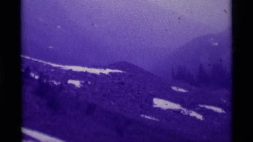1975 Montana 8mm view of foggy mountain slopes, scattered snow, and evergreen trees with visible film borders.