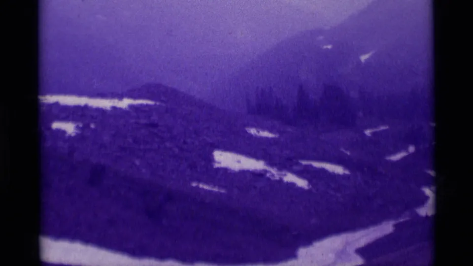 1975 Montana home-movie frame showing a fog-softened mountain ridge, snow patches, and evergreen trees.