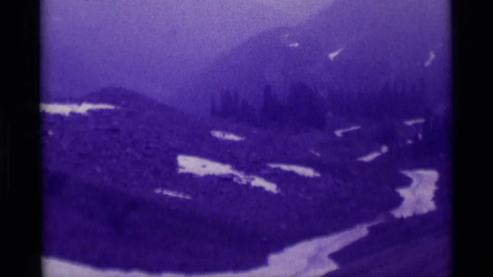 1975 Montana 8mm frame of a sloping forest landscape with melting snow and low mountain haze.
