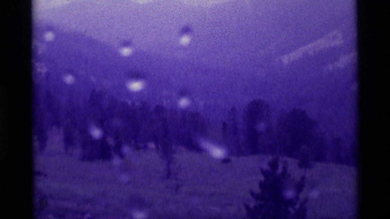 Rain-specked view of distant mountains and trees through a purple-tinted 8mm frame.
