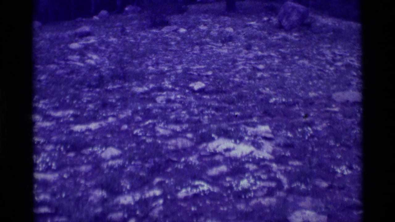 1975 Agate Springs, Montana 8mm frame showing uneven rocky terrain under a dense purple cast, with no people or structures visible.