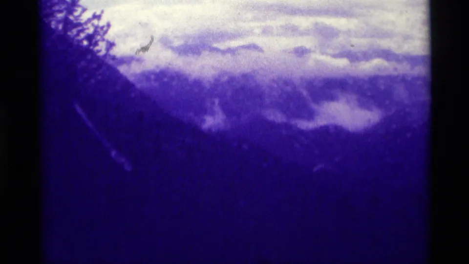 Archival 8mm frame from Agate Springs, Montana, showing cloud-covered mountain terrain under a strong blue-purple cast.