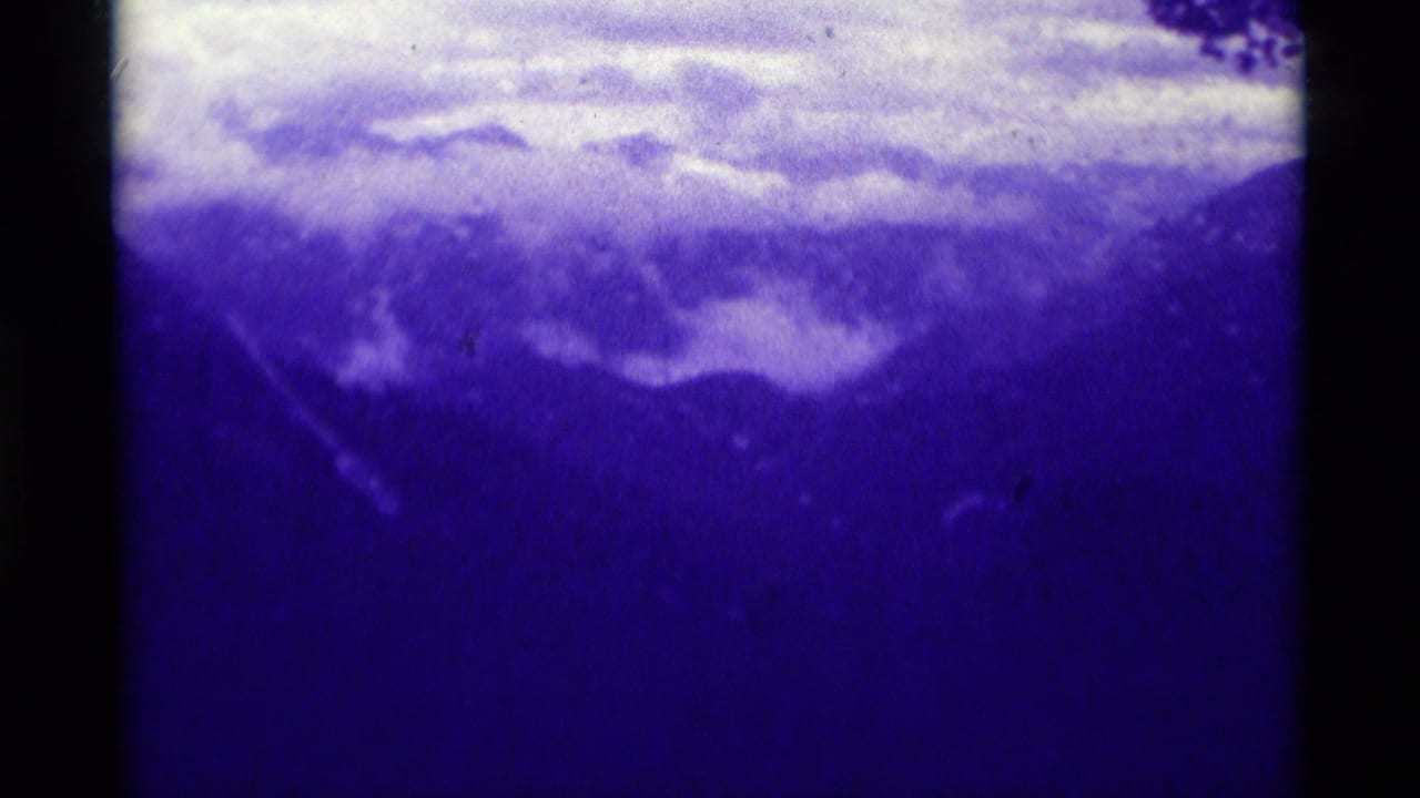 1975 8mm Montana landscape frame showing layered mountains, low clouds, and dense blue film color shift.