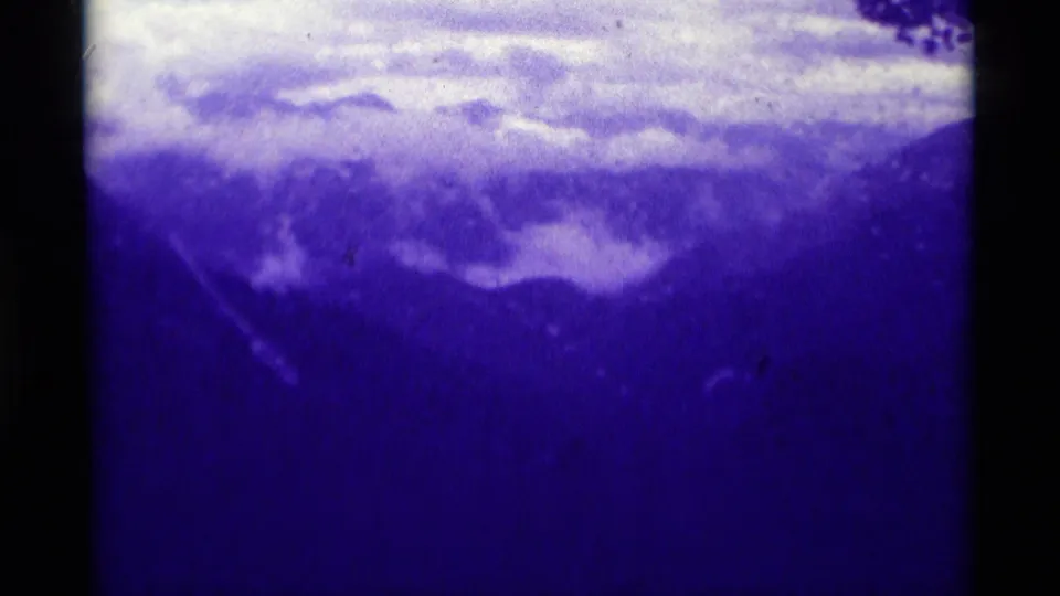1975 8mm Montana landscape frame showing layered mountains, low clouds, and dense blue film color shift.