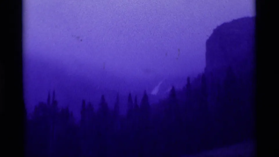Purple-cast 8mm frame showing forest silhouettes, open sky, and a steep mountain or rock form in the Montana landscape.