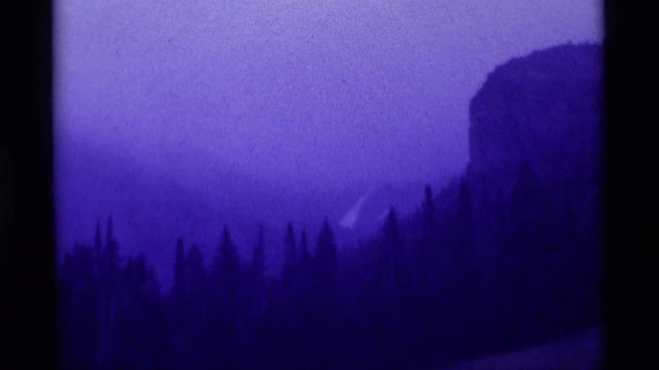 1975 8mm Agate Springs, Montana view of evergreens below a misty mountainside with a cliff-like rise at right.