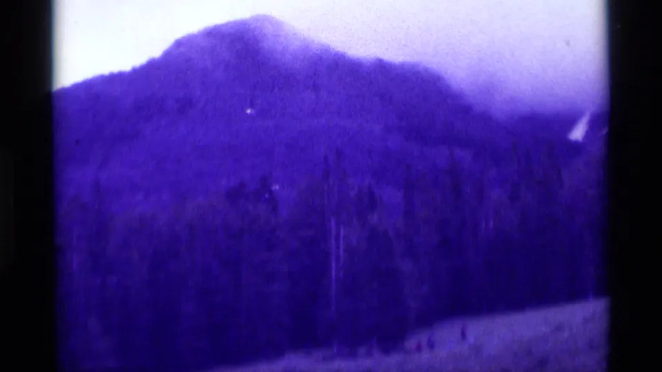 1975 8mm Agate Springs, Montana view of a rounded forested mountainside with tiny people visible along the lower pale area.