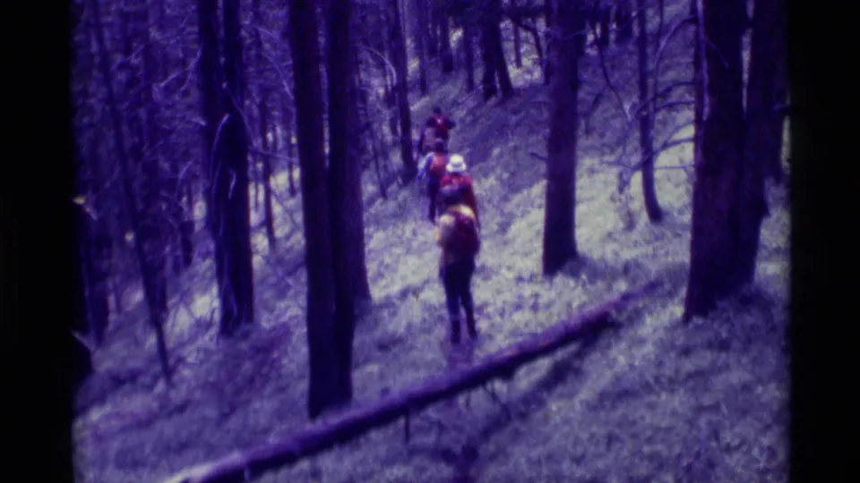 1975 8mm home-movie frame of a small hiking group moving away through trees in Agate Springs, Montana.