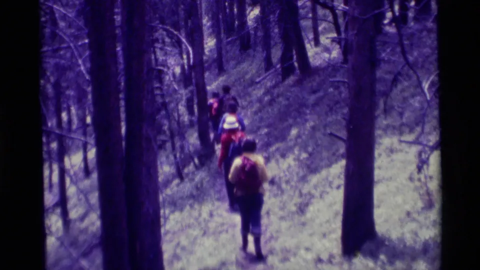 The hiking group appears closer in this 1975 home-movie frame, walking through tall trees with backpacks visible.