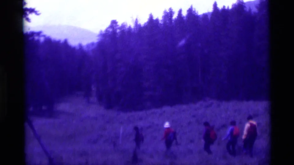 A wider 8mm view shows hikers moving through a Montana meadow, with dense trees and distant terrain behind them.