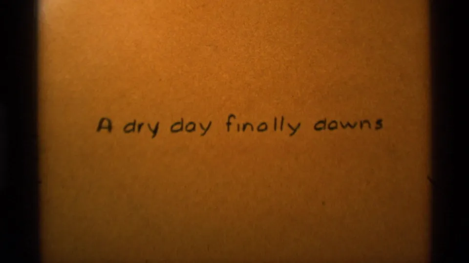 Handwritten title card on tan paper, part of the 1975 Agate Springs 8mm home movie, reading A dry day finally downs.