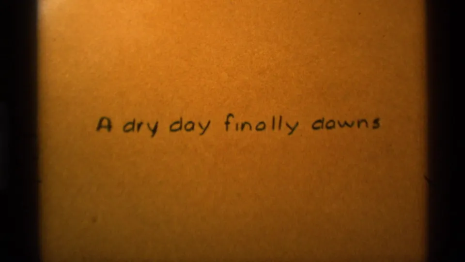 Close view of the 8mm handwritten title card on textured tan paper, reading A dry day finally downs.