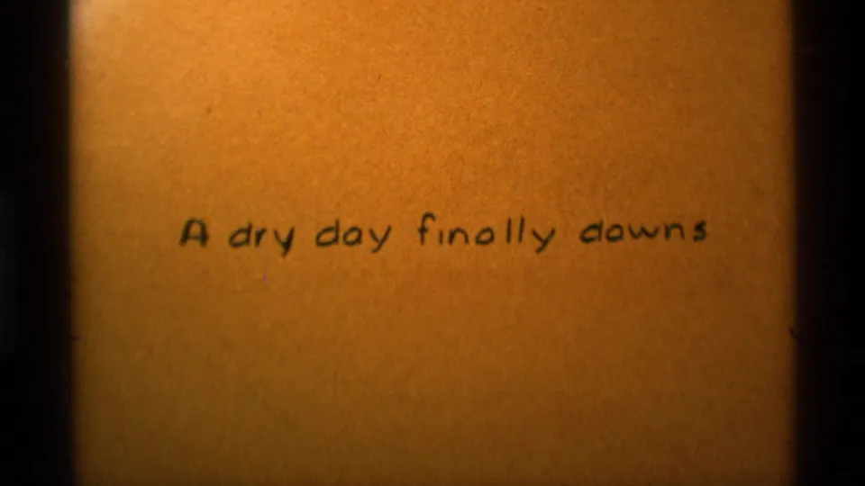 Final 8mm frame holds on the handwritten title card, centered on tan textured paper with dark edge vignetting.