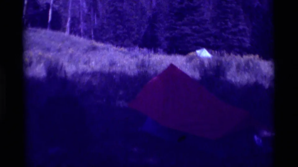 Red tent appears in a grassy field near a tree line in the 1975 Agate Springs, Montana home-movie footage.