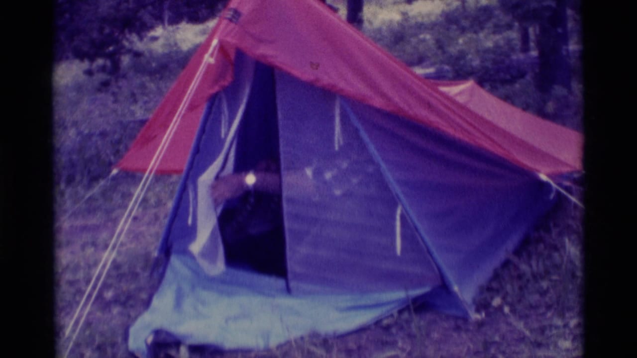 1975 8mm frame from Agate Springs, Montana showing a red and purple tent in woods before the camper emerges.