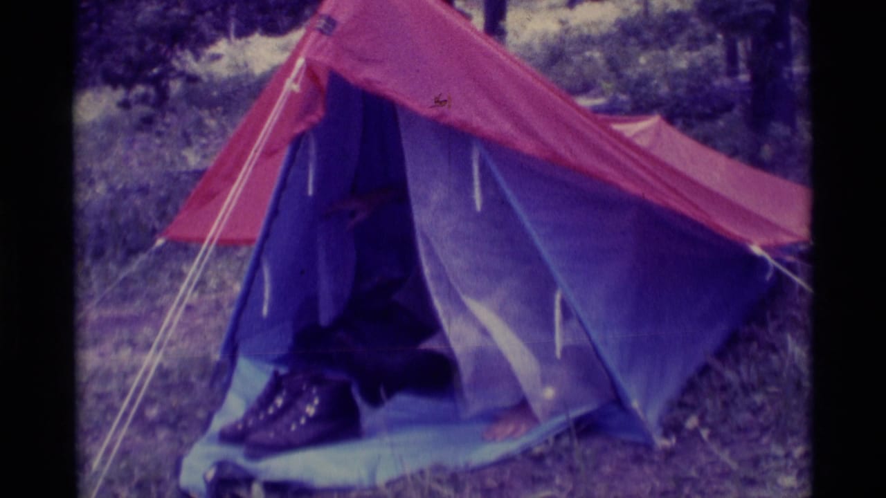A man begins to appear in the open entrance of a red and purple tent.